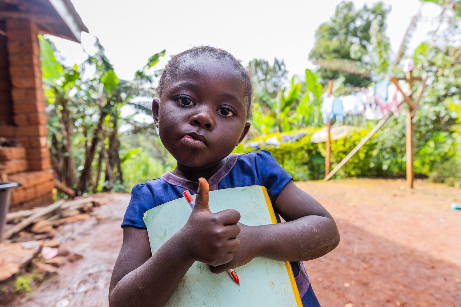 Joyful young black toddler holding a book and a pen with thumbs up