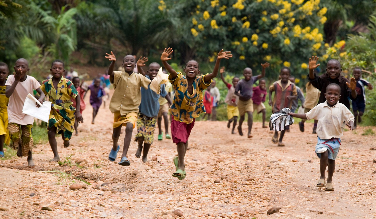 Joyful children running down a dirt road amidst vibrant flora